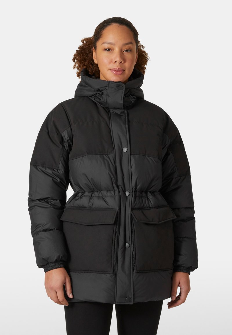 Zwarte gewatteerde jas met een trekkoord capuchon, knoopsluiting, twee grote voorzakken en elastische manchetten. Heeft een getailleerde taille voor een goede pasvorm.