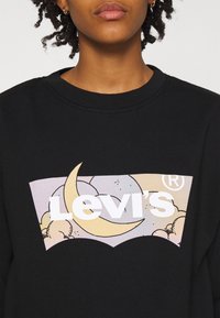Sweat-shirt noir avec un grand motif pastel de nuages et de lunes, affichant en évidence le logo blanc « Levi's ». Texture en coton doux.