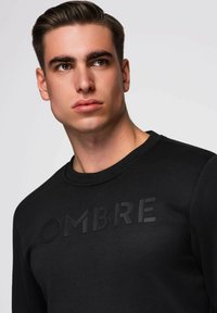 Czarna bluza z teksturowanym napisem „OMBRE” na piersi. Posiada okrągły dekolt i ściągacze, wykonana z gładkiego, miękkiego materiału.