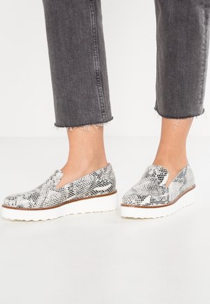 Czółenka wsuwane w czarno-białym wzorze węża, z fakturowaną górną częścią i białą platformą z falistą krawędzią.