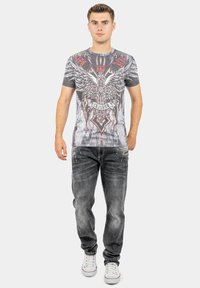Grijze grafische t-shirt met een adelaarontwerp en rode accenten, gecombineerd met vervaagde grijze jeans en witte sneakers.