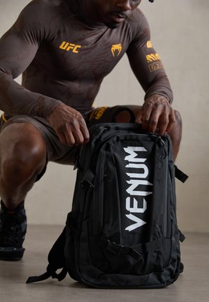 Black backpack with "VENUM" in large white letters on the front. Features multiple zippers, side pockets, and adjustable straps.