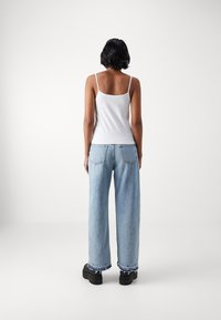 Hvit, tettsittende tanktopp med tynne stropper, sammen med lyseblå, løstsittende bukser med slitt kant og baklommer. Svarte plattformsko.