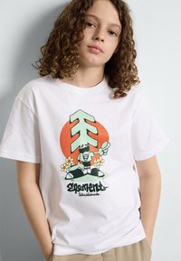 Witte katoenen t-shirt met een kleurrijk grafisch ontwerp van een cartoonfiguur, geometrische vormen en florale accenten. Casual pasvorm, korte mouwen.