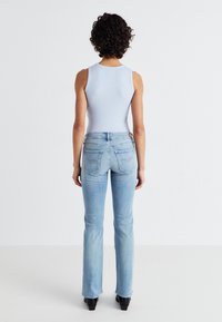 Lichtblauwe mouwloze top gecombineerd met een medium gewassen flared jeans met achterzakken en een klein merketiket op de tailleband.