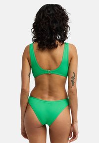 Σετ πράσινου μπικίνι από λείο υλικό. Το πάνω μέρος έχει φαρδιές τιράντες και ανοικτή πλάτη, ενώ το κάτω μέρος διαθέτει κλασικό ψηλοκομμένο σχέδιο.