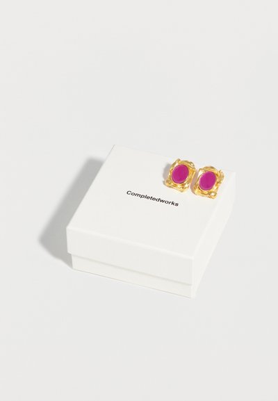 Σκουλαρίκια σε χρυσό τόνο με οβάλ, φωτεινά ροζ πέτρες, τοποθετημένα πάνω σε ένα λευκό κουτί κοσμημάτων Completedworks σε λευκό φόντο.