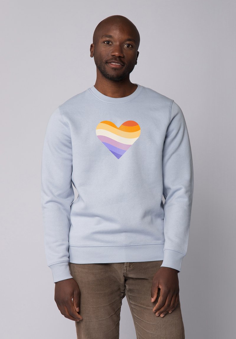 Lichtblauwe sweatshirt met een hartafbeelding met horizontale strepen in oranje, geel, crème, paars en lavendel. Gladde textuur.