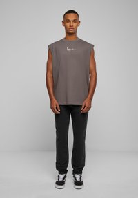 Pilkos be rankovių medvilninės marškinėliai laisvu siluetu, su logotipu ant krūtinės. Su derančiomis juodomis kelnėmis ir juodai baltomis sportinėmis bateliais.