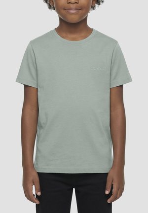 Kind draagt een lichtgroen T-shirt met korte mouwen met een klein wit logo op de linkerborst en zwarte broek, tegen een effen grijze achtergrond.