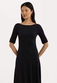 Black dress with an off-the-shoulder neckline, fitted bodice, and rolled sleeves. Fabric appears soft with a smooth texture.