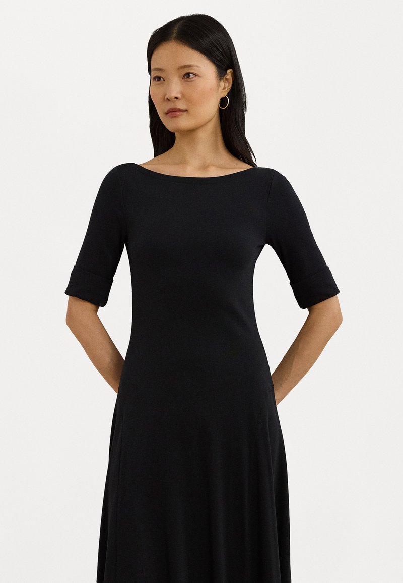Black dress with an off-the-shoulder neckline, fitted bodice, and rolled sleeves. Fabric appears soft with a smooth texture.