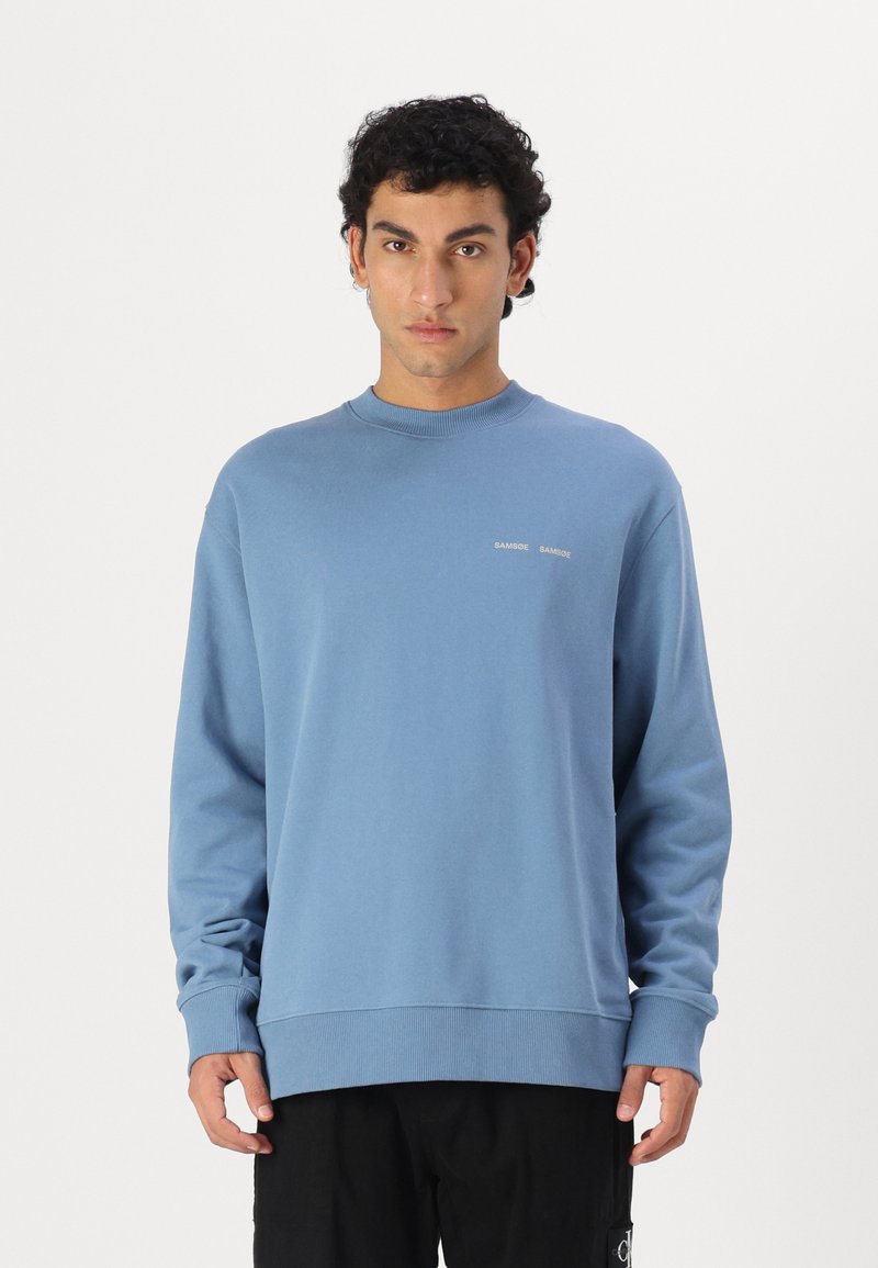 Blue cotton sweatshirt with long sleeves, ribbed cuffs and hem, featuring a small logo on the chest. Smooth texture and relaxed fit.