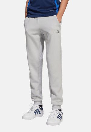 Un pantalon de survêtement gris au design ajusté, avec des poches latérales et un logo ton sur ton subtil. Associé à des baskets blanches avec des rayures bleues.