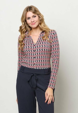 Blouse met lange mouwen met een geometrisch patroon in rood en marineblauw, een knoopsluiting bij de V-hals en een comfortabele pasvorm, gecombineerd met marineblauwe broek.