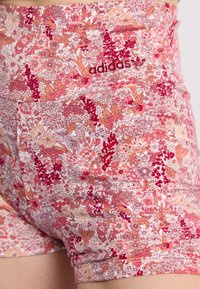 Gėlėmis raštuoti rožinės ir koralinės spalvos sportiniai šortai su elastinga juosta bei siuvinėtu tamsiai raudonu Adidas logotipu. Pagaminti iš lygios, tamprios medžiagos.