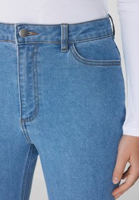 Jeans de talle alto en azul claro, hechos de mezclilla, con costuras naranjas, bolsillos frontales y cierre de botón metálico en la cintura.
