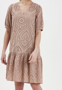 Světle růžové šaty vyrobené z broderie anglaise látky, s V-výstřihem, krátkými puff rukávy a rozšířenou sukní se nařaseným lemem.