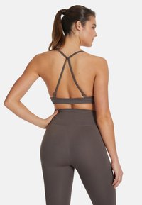 Urheiluliivit tummanharmaasta, ribatusta kankaasta, jossa on ristiselkädesign ja säädettävät olkaimet, yhdistettynä korkeavyötäröisiin legginsseihin.