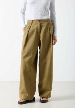 Pantaloni a vita alta, a gamba larga, color verde oliva, realizzati in tessuto strutturato, con pieghe frontali, tasche laterali e chiusura con bottone.