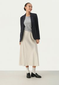 Jūras flotei raksturīga pinstripe žakete virs pelēka T-kreklu, ko papildina krēmkrāsas midi svārki. Melni loafers un baltas virsceļgalu zeķes noslēdz kopējo izskatu.