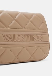 Vadderad beige läderhandväska med präglad "VALENTINO" logotyp. Har diamantmönster och detaljer med kontrasterande sömmar.