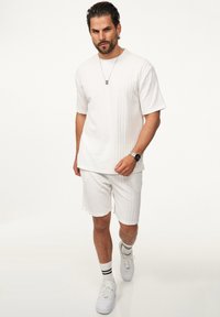 White ribbed short-sleeve shirt and matching shorts, made of textured fabric. Worn with white sneakers and striped socks. Silver necklace present.