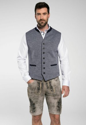 Grauer Stoffwesten mit Knopfleiste und marineblauen Akzenten, kombiniert mit beigen Leder-Shorts mit floralem Stickmuster und dekorativen Knöpfen.