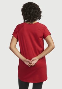 Rød bomuld t-shirt med korte ærmer og en afslappet pasform. Let buet forneden og raglanærmedesign. Bæres med sorte leggings.