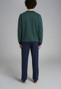 Felpa verde a pois con polsini navy abbinata a pantaloni navy. Il tessuto sembra morbido e comodo, progettato per l'abbigliamento da casa.