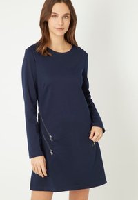 Vestido de manga larga en color marino, confeccionado en una tela suave. Cuenta con un escote redondo y dos bolsillos con cremallera a cada lado para un detalle adicional.