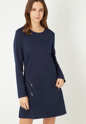 Vestido de manga larga en color marino, confeccionado en una tela suave. Cuenta con un escote redondo y dos bolsillos con cremallera a cada lado para un detalle adicional.