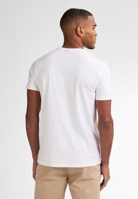 Camiseta blanca de algodón con mangas cortas, que presenta un cuello redondo básico y un corte relajado. La tela parece suave con un detalle mínimo.