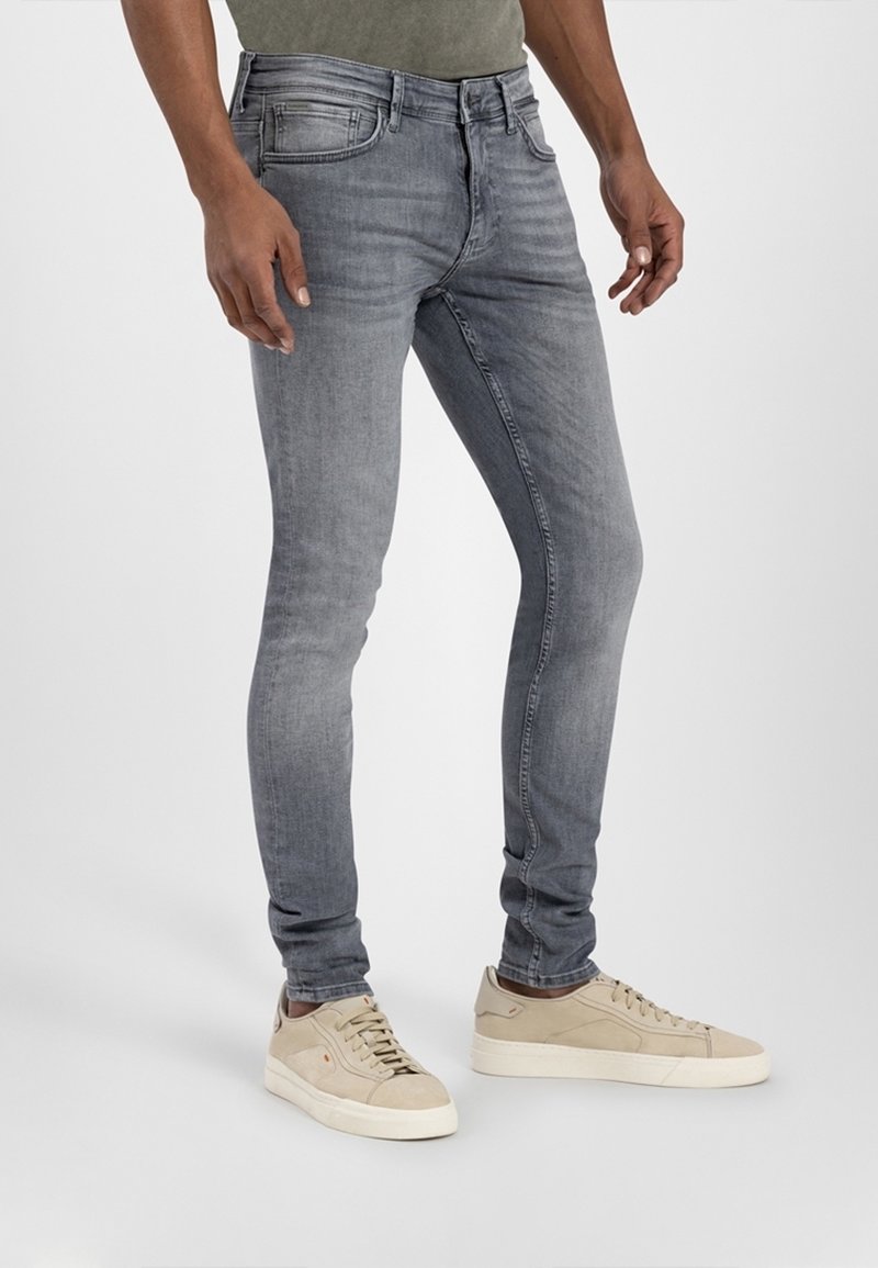 Schmal geschnittene graue Jeans aus Denim mit einem verwaschenen Finish, Fünf-Taschen-Design und gestickten Details, kombiniert mit hellen Sneakers.