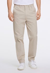 Beige chinos med avslappnad passform, med knappstängning, framveck och sidofickor, matchade med vita sneakers. Slät textur.