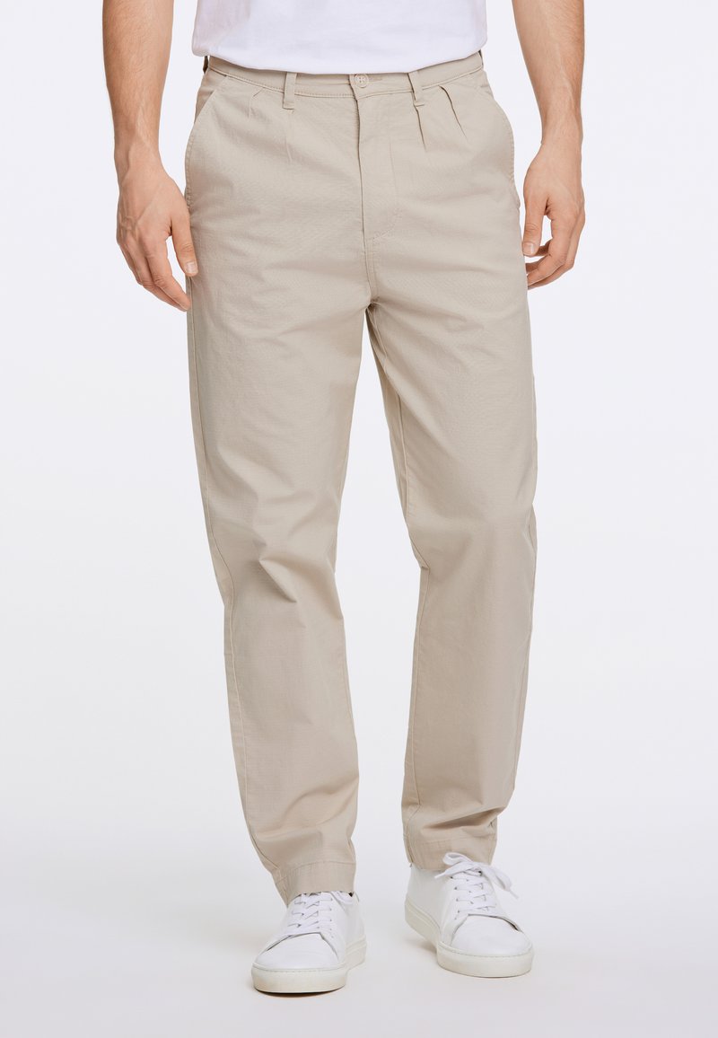 Beige chinos med avslappnad passform, med knappstängning, framveck och sidofickor, matchade med vita sneakers. Slät textur.