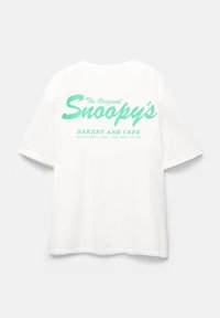 Bílý bavlněný tričko s zeleným textem na zadní straně, který zní "The Original Snoopy's Bakery and Cafe" s dalšími detaily níže.