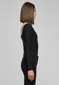 Svart ribbestrikket bodysuit med lange ermer og åpen ryggdesign, sammen med høyt midje svarte jeans. Glatt tekstur og tettsittende silhuett.