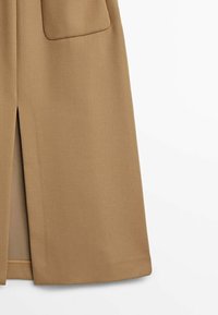 Vaa beige villasekoite takki suoran leikkauksen kanssa, jossa on etu halkio ja kaksi läpällistä taskua. Sileä pinta, minimalistinen muotoilu, ei näkyvää metalliosaa.