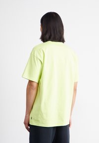 Limegrön bomullströja med korta ärmar, avslappnad passform och rund hals. Finns med sidoflikka. Enfärgad bakvy.