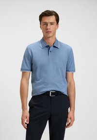 Ljusblå pique-shirt med krage, med en kontrasterande vit kant. Kombinera med marinblå byxor och ett svart bälte.