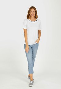 Weißes T-Shirt mit kurzen Ärmeln, das einen schwarz-weißen gemusterten Halsausschnitt aufweist, kombiniert mit hellblauen cropped Jeans und schwarz-weiß gestreiften Schuhen.