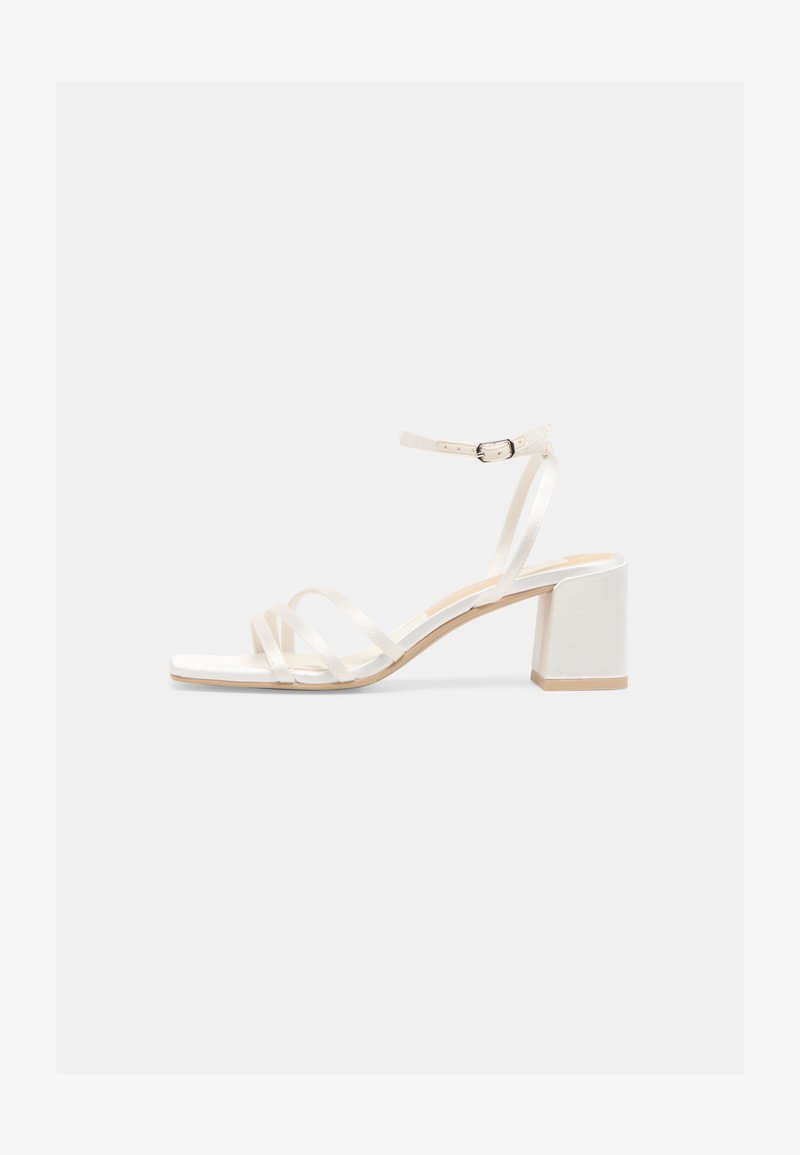 Λευκό σανδάλι ανοιχτού δαχτύλου με λεπτούς ιμάντες, λουρί στον αστράγαλο με πόρπη και μεσαίο τετράγωνο τακούνι σε απλό φόντο.