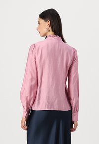 Rosa langermet bluse med rynket halslinning og puffede ermer. Knapper i mansjettene, glatt tekstur, nederkanten faller rett over livet.