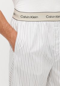 Witte gestreepte katoen pyjamabroek met een beige elastische tailleband waarop 'Calvin Klein' in het zwart is gedrukt. Inclusief zijzakken.