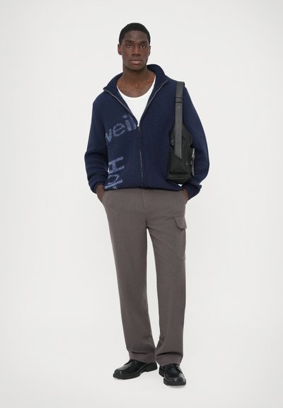 Marininspirerad zip-up tröja med textmönster, grå cargobyxor och svarta skor. Accessoar: svart axelväska med justerbar rem.