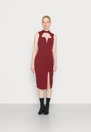 Vestido borgonha sem mangas com decote alto, recorte em formato de olho-chave e fenda lateral. Tecido suave e corte justo. Combinado com botas pretas até ao tornozelo.