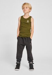 Olijfgroene tanktop met een logo, gecombineerd met losse zwarte joggingbroek en zwarte hoge sneakers met accenten. Eenvoudig en sportief design.
