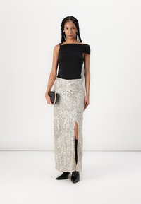 Črna off-shoulder majica v kombinaciji s srebrno bleščečo maksi krilo z visokim razporkom, dopolnjena z črnimi gležnjarji in majhno torbico.