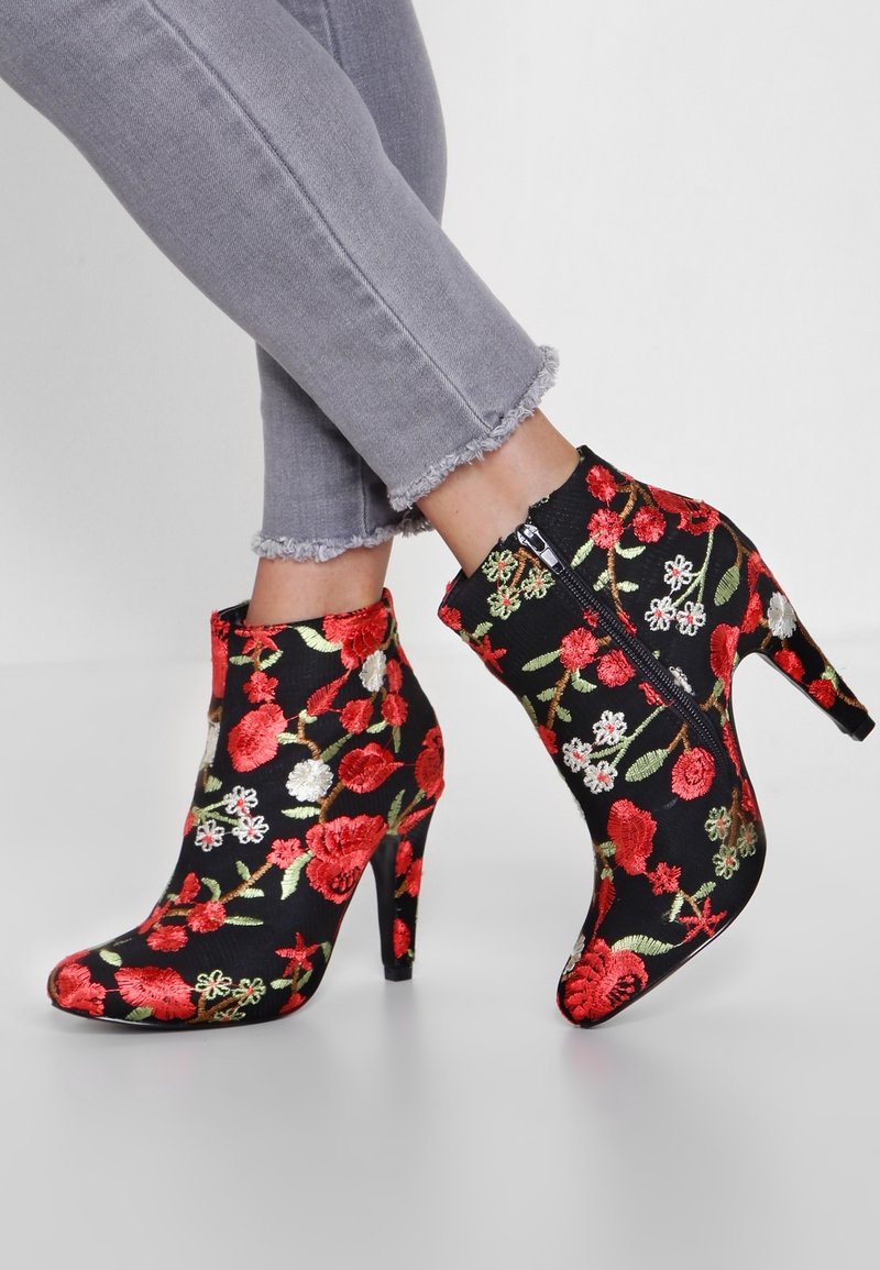 Schwarze Ankle-Boots mit hohem Absatz, ausgestattet mit buntem Blumenstickerei in Rot, Grün und Weiß, und einem seitlichen Reißverschluss.